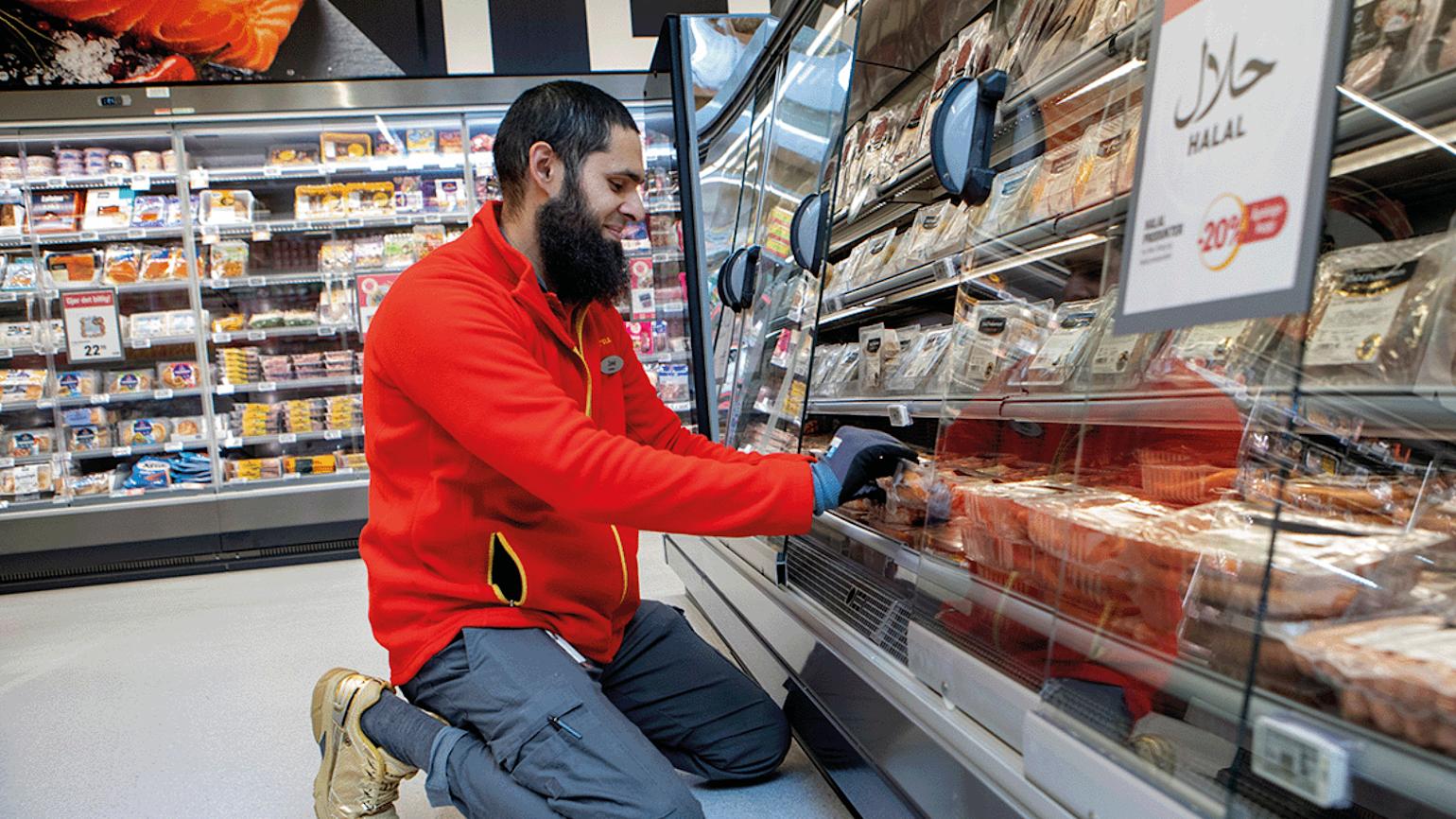 Mann sitter på hun og pakker ut varer i Extra butikk.