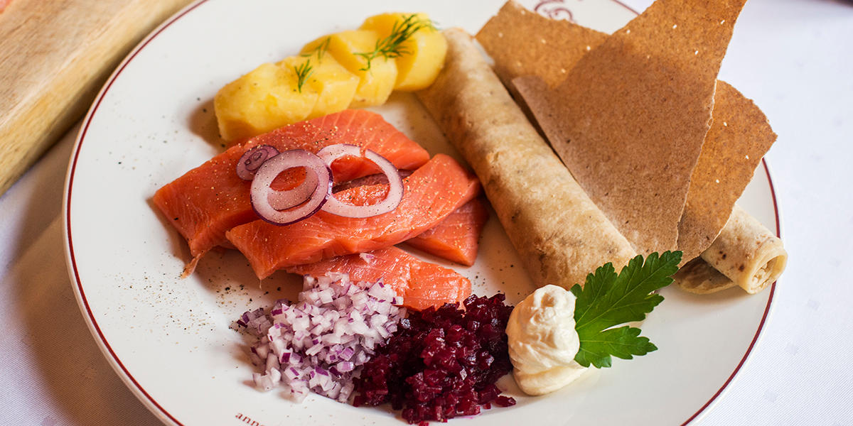 Tradisjonell rakfisk a la Engebret Café servert på hvit tallerken med klassisk tilbehør som lefser, flatbrød, rømme, kokt potet, rødløk og rødbete.
