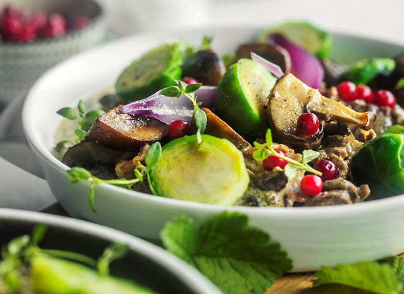 Finnbiff servert i hvit skål, med sopp, rosenkål, rødløk og ferske tyttebær på toppen.