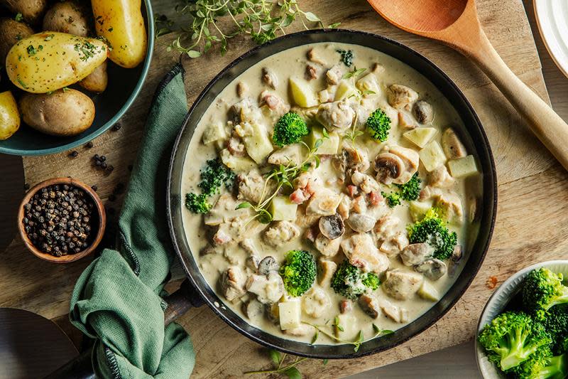 Stor lun kjele med kremet kyllinggryte servert på trefjøl. Kokte poteter og brokkoli servert på siden. 