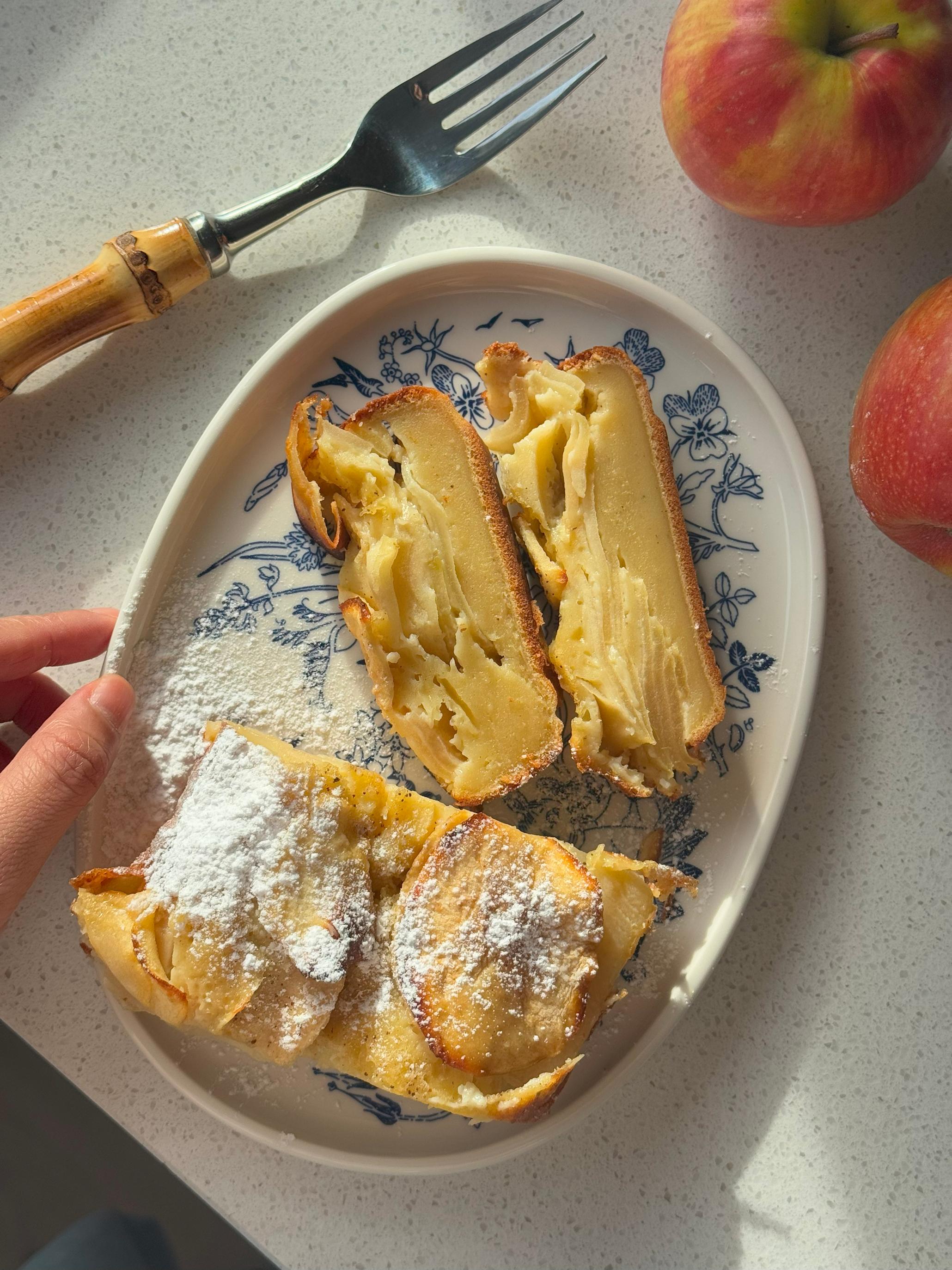 Usynlig eplekake - eplekake med tynne skiver epler bakt inn i deigen, servert på hvitt og blåmønstret fat. Friske epler og gaffel med bambusskaft ved siden av.