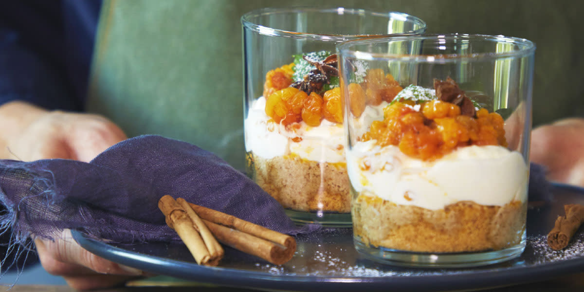 Ostekake i glass med julekrydrede multer og pepperkakebunn, pyntet med stjerneanis, sitronmelisse og melisdryss. Glassene er servert på fat med lilla linserviett og hele kanelstenger.