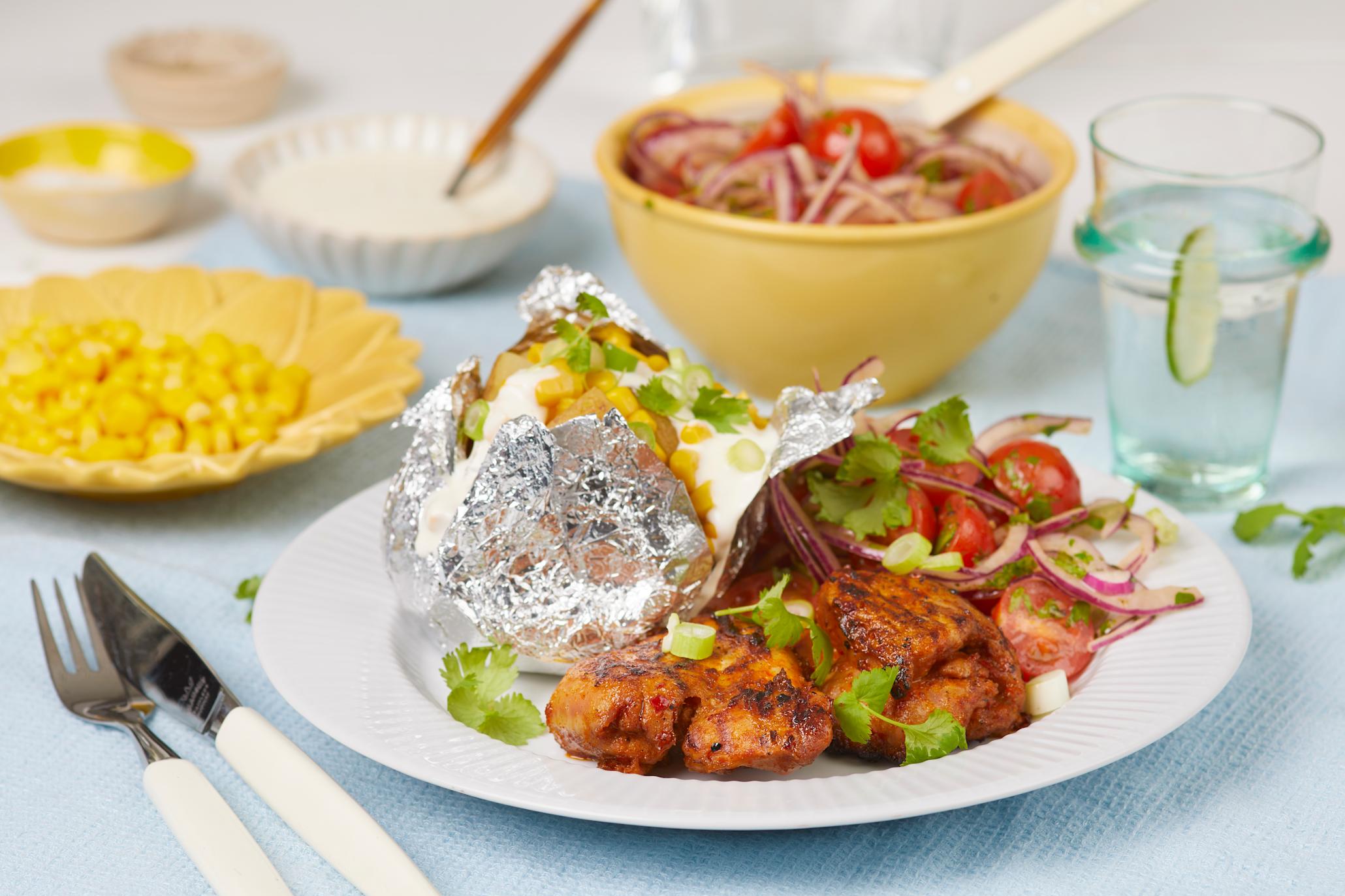 Lårfilet Smokey BBQ med bakt potet og rømmedressing på en stor hvit tallerken med en gul tallerken med mais og en gul bolle med løksalat