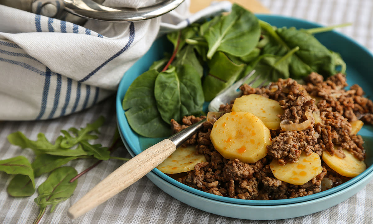 Gryterett med poteter og karbonadedeig sammen med salat og en gaffel, servert på en blå tallerken.