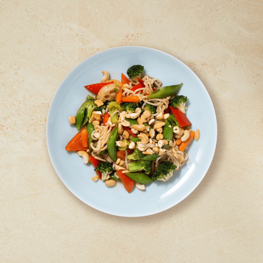 Vegetarwok med nudler, nøtter og masse grønnsaker, servert på en lys blå tallerken