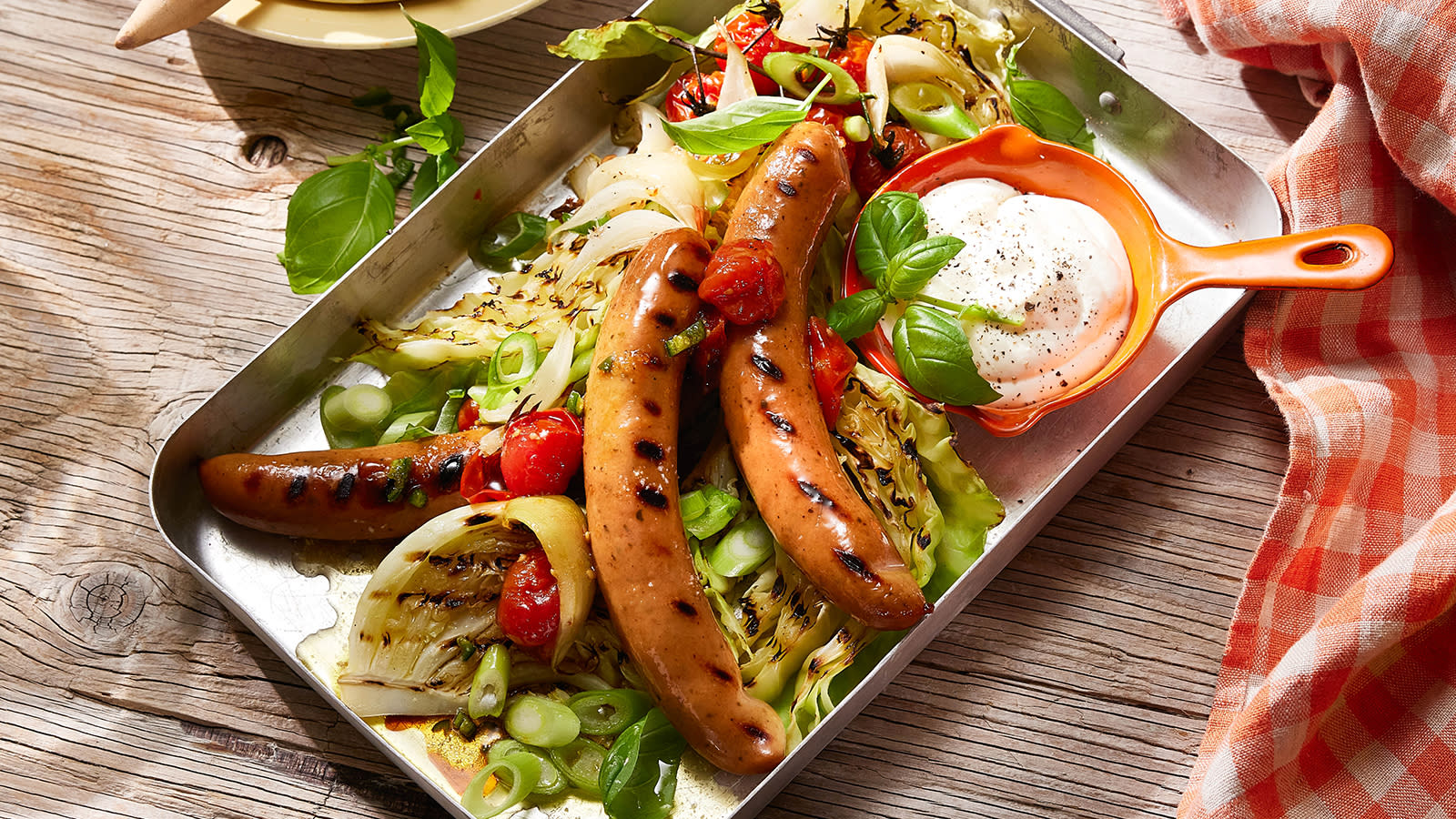 Bratwurst med tomatrelish og grillet nykål servert i stekeform av metall med en oransje skål med aioli ved siden av.