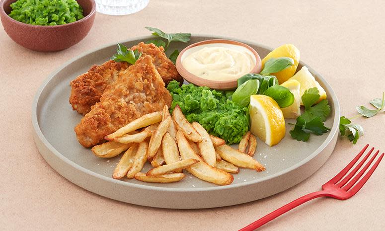 Crispy fish and chips på tallerken med ertepuré, sitronbåter, ferske urter og remulade. Lys bakgrunn.