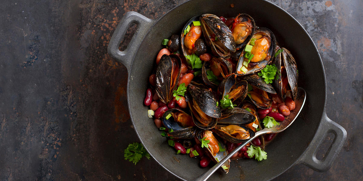 Blåskjell med bønner og chorizo tilberedt på grillen, og servert i svart jerngryte med friske urter over.