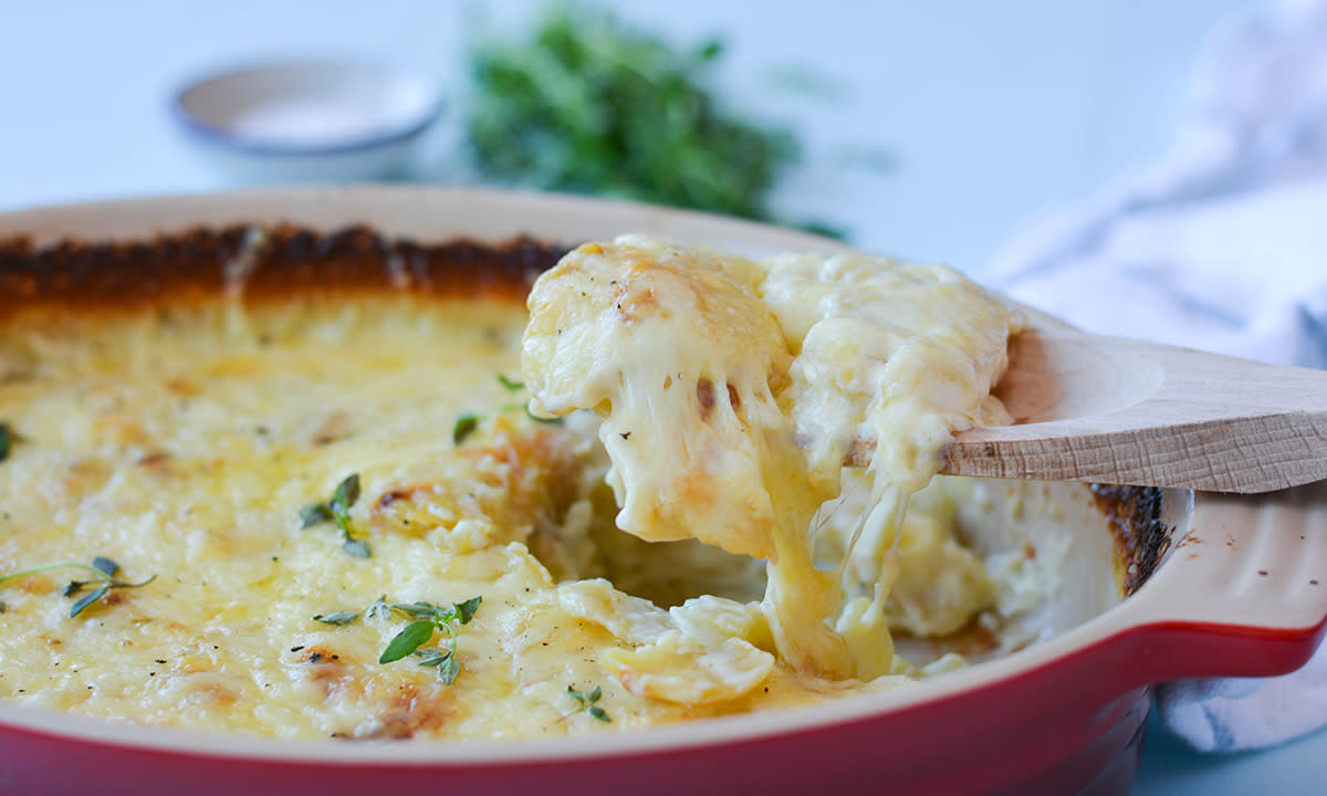 Fløtegratinerte poteter i rød ildfast form. Potetene er dekket av smeltet ost.