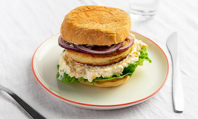Fiskeburger med rødløk, salat og yoghurtdressing på en hvit tallerken med rød kant.