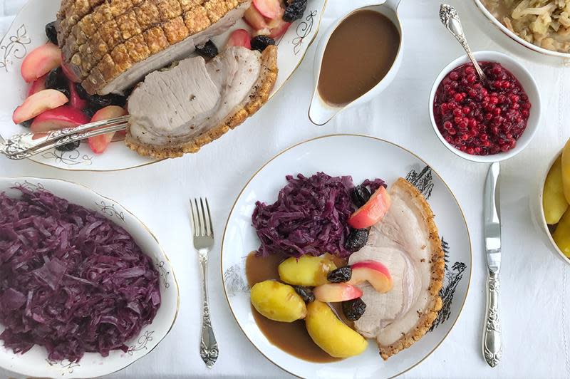 Svinestek med sprø svor, på en seng av bakte epler og svisker. Servert med surkål og rødkål, på klassisk pent dekket bord med hvit duk.