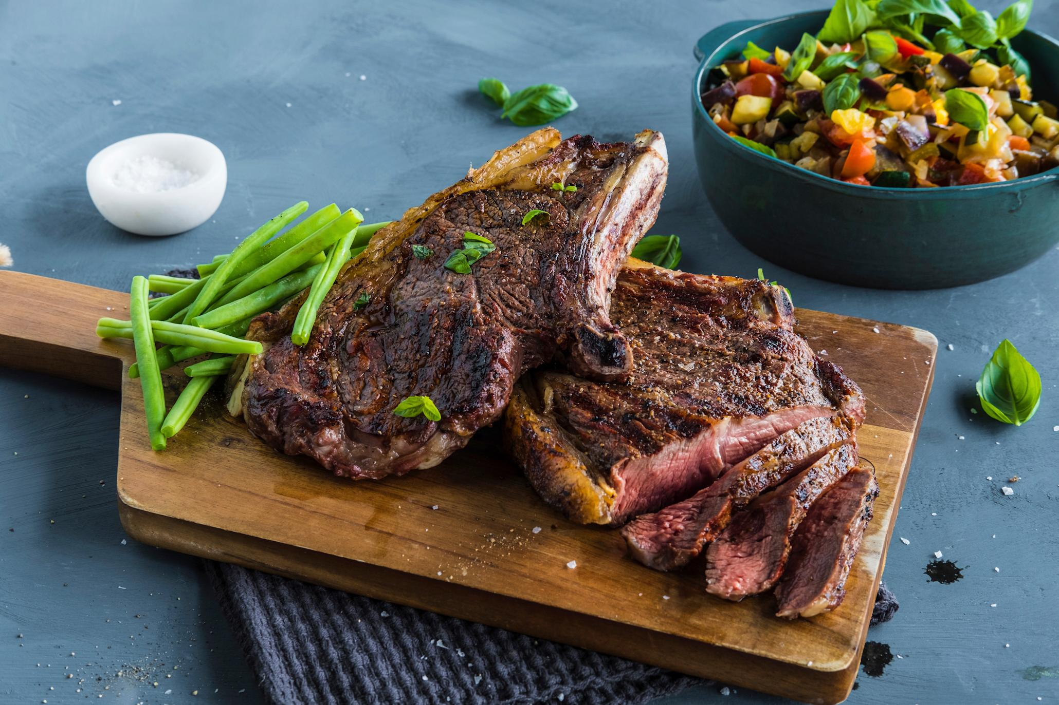 Entrecote og aspargesbønner på et trefat og en skål med ratatouille ved siden av