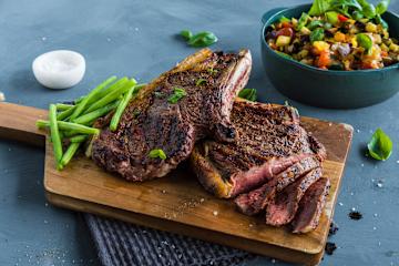 Entrecote og aspargesbønner på et trefat og en skål med ratatouille ved siden av