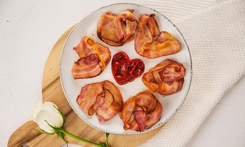 Hjertebacon i ovnen, baconstrimler formet til hjerter og stekt i stekeovnen. Servert på hvit frokosttallerken med hjerteformet ketchup i midten.