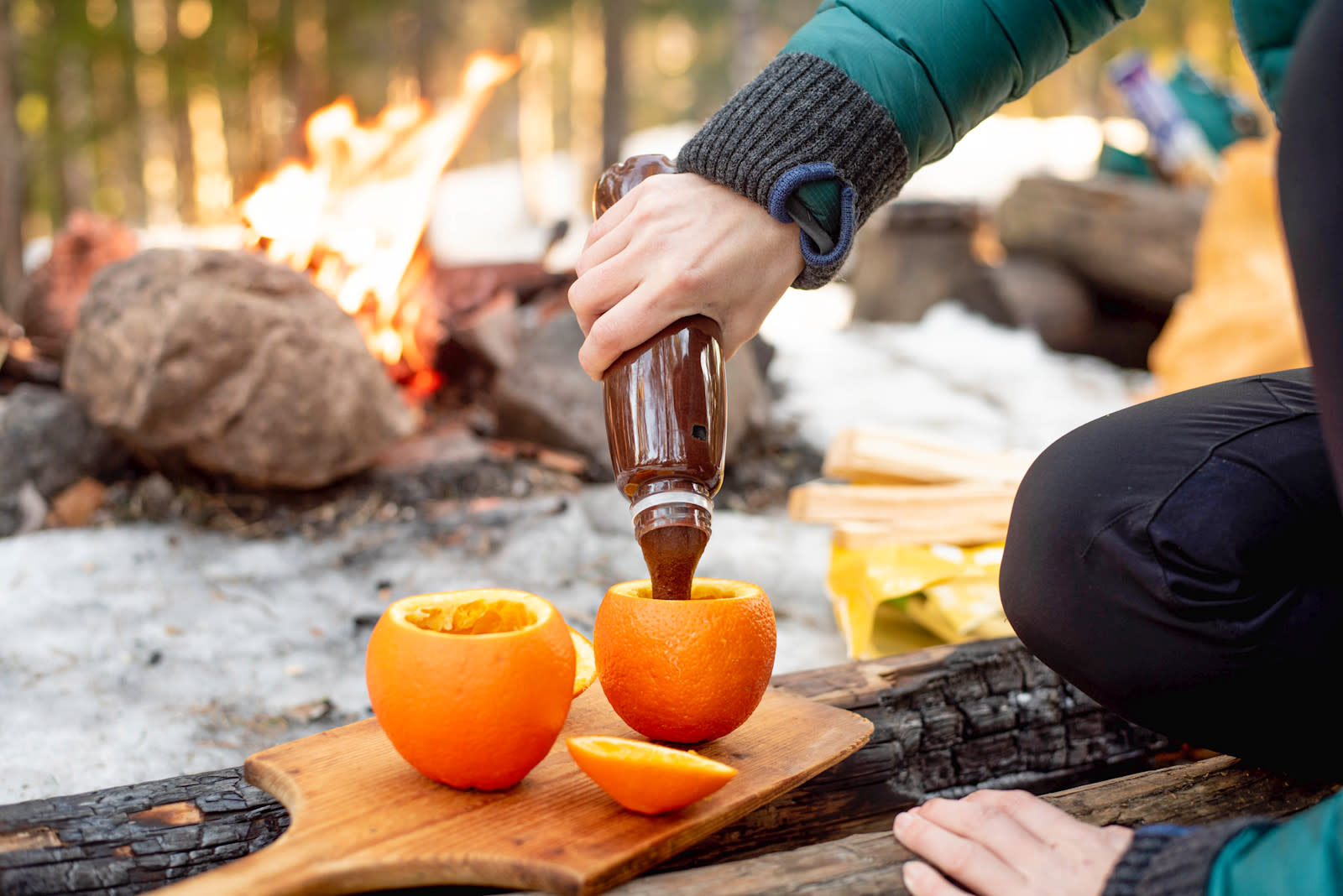 Brownies i appelsin - på bålet. Brownierøre helles i hule appelsiner på trefjøl. Bål i bakgrunnen.