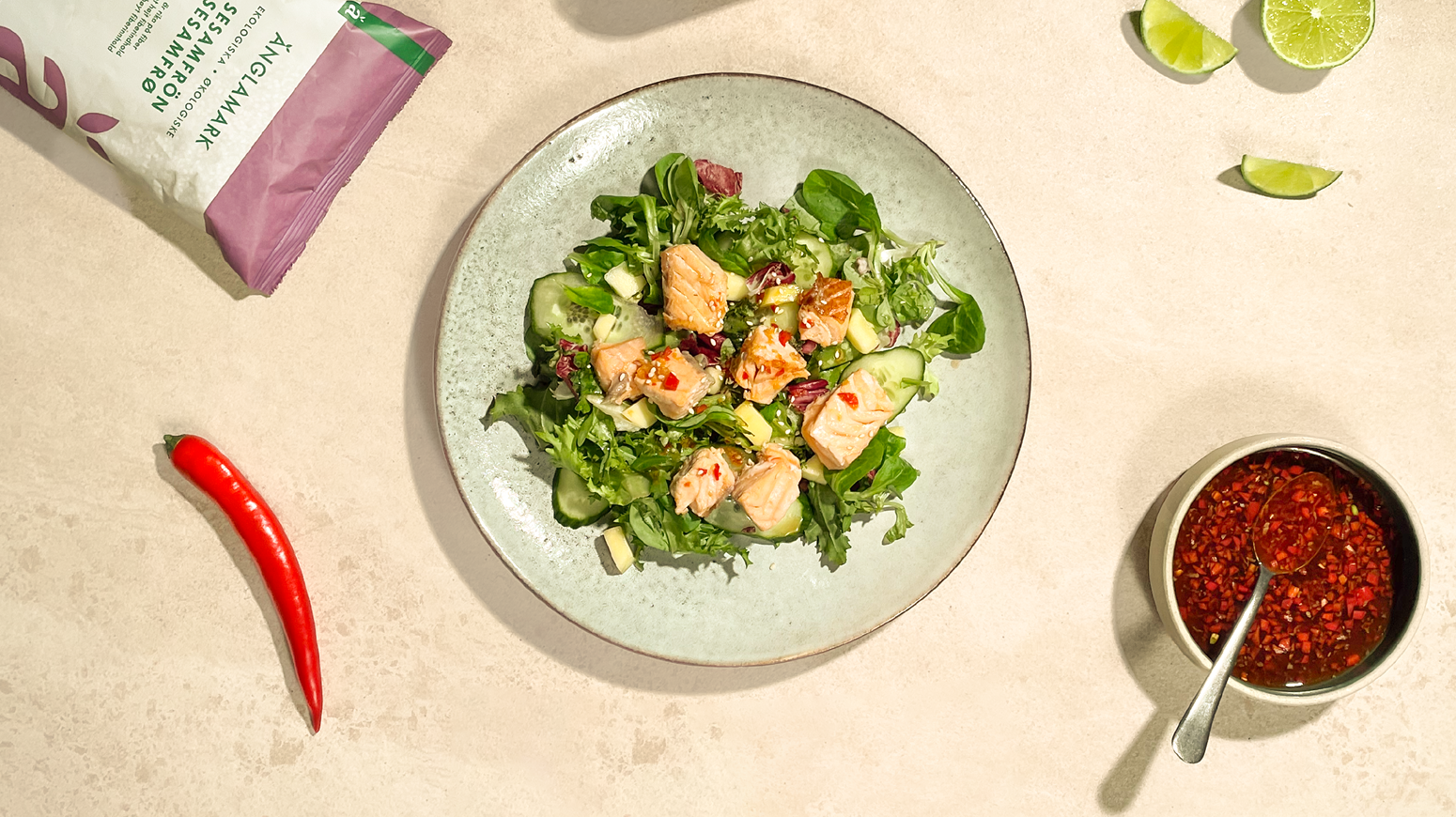 Asiatisk laksesalat med lime, chili, sesamfrø og asiatisk dressing servert på lys grønn tallerken, på lys bakgrunn.