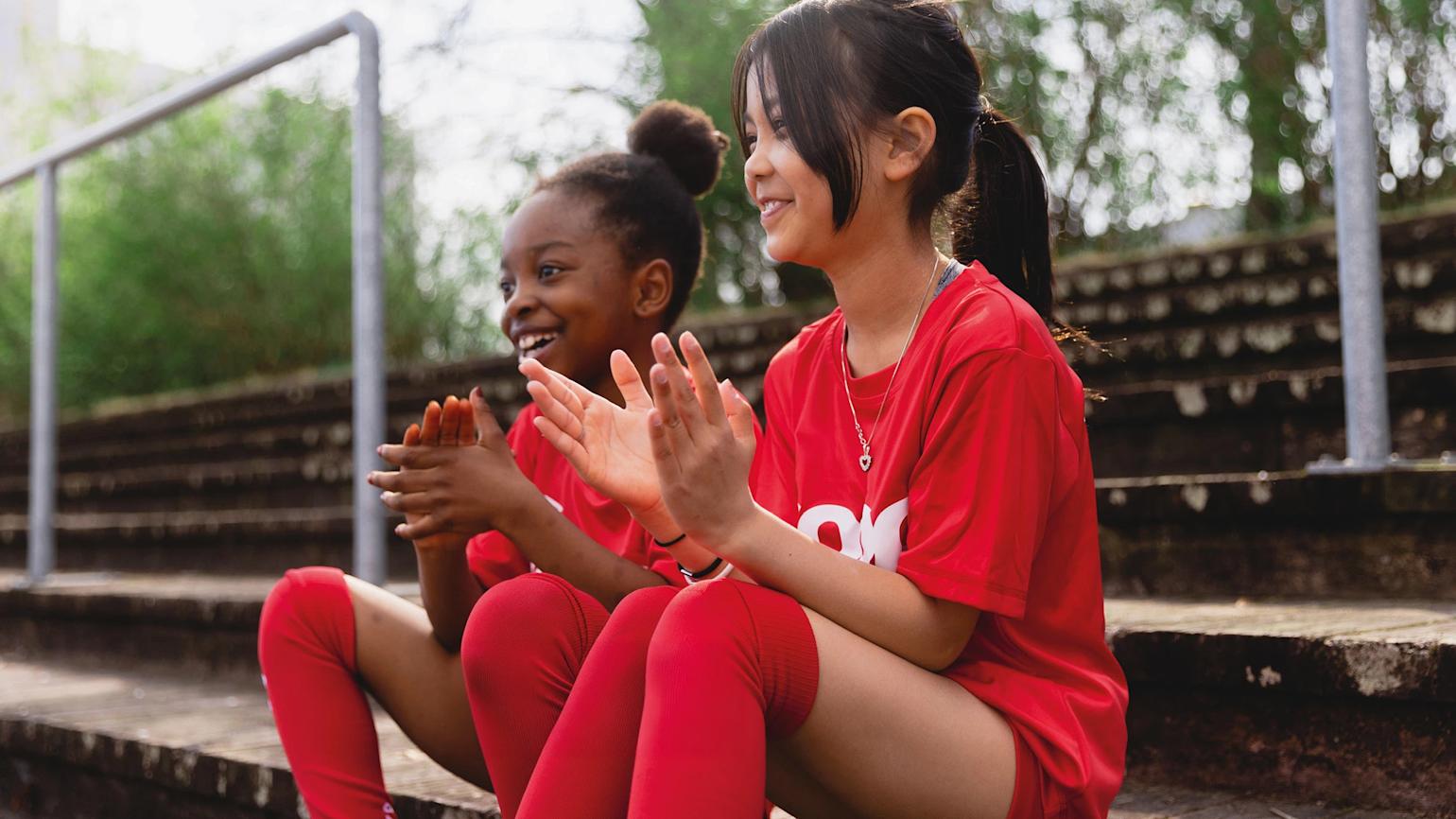 To jenter sitter på tribune med Coop drakter