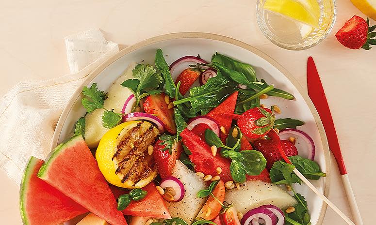 Jordbær- og melonsalat, med babyleaf, grillet sitron, koriander og rødløk på hvit tallerken. Lys bakgrunn.