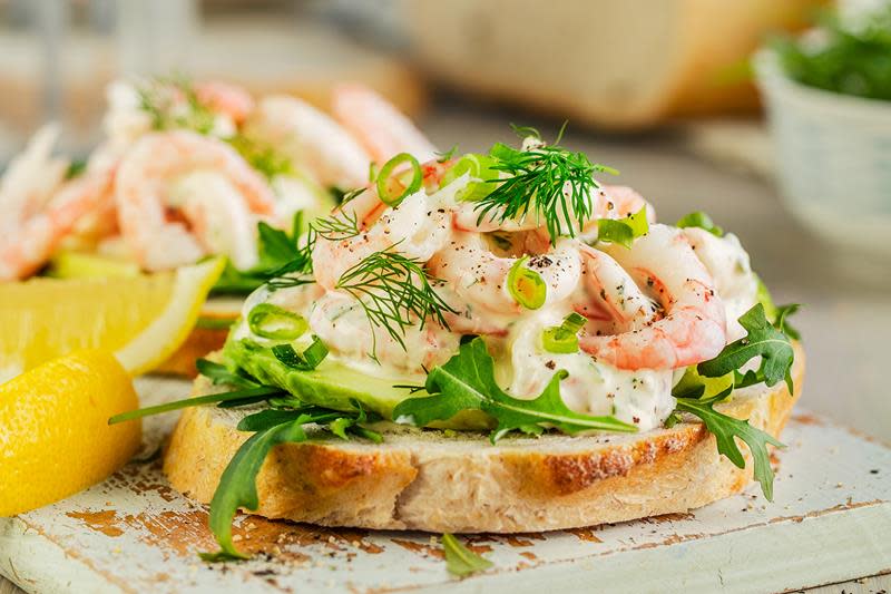 Loffskive med ruccolasalat og kremet rekesalat laget av ferske reker. Sitronbåter ved siden. Hvit trefjøl.