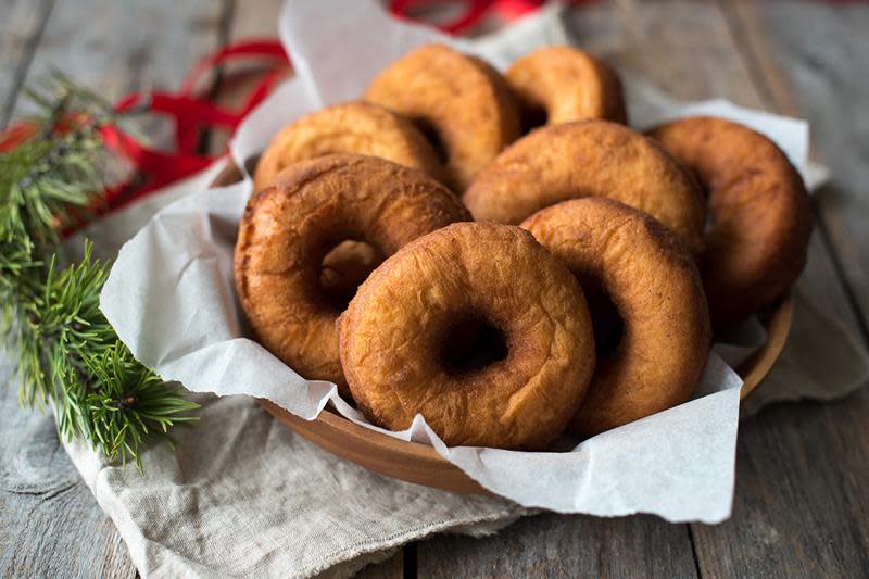 Hjemmelagede smultringer servert i rund trekurv på lys linserviett på rustikk trebord. Rødt julebånd og granbar rundt.