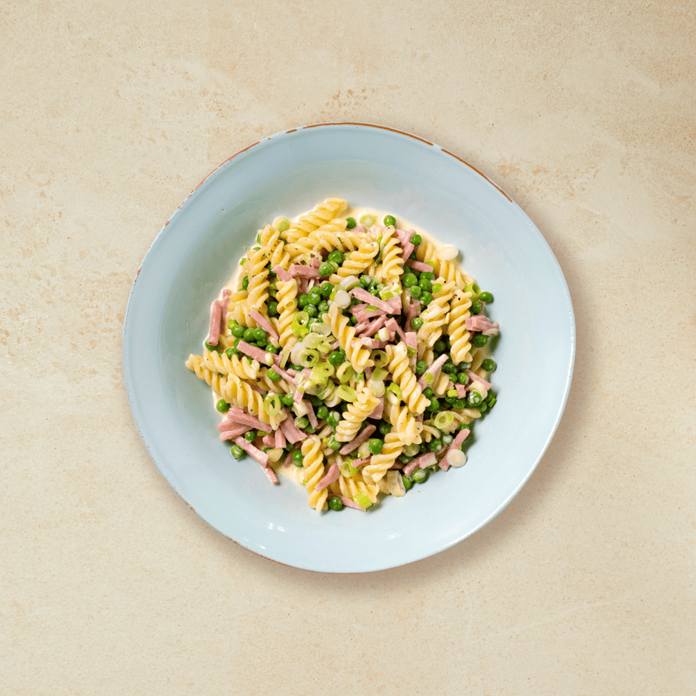 Pasta med fløtesaus, skinke, erter og vårløk i en lys blå skål