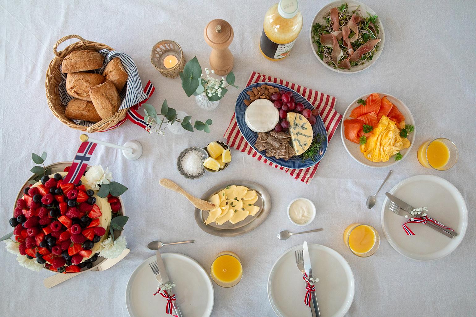 17. mai pyntet frokostbord sett ovenfra med juice, kake, eggerøre, skinke, laks, rundstykker, smør osv.