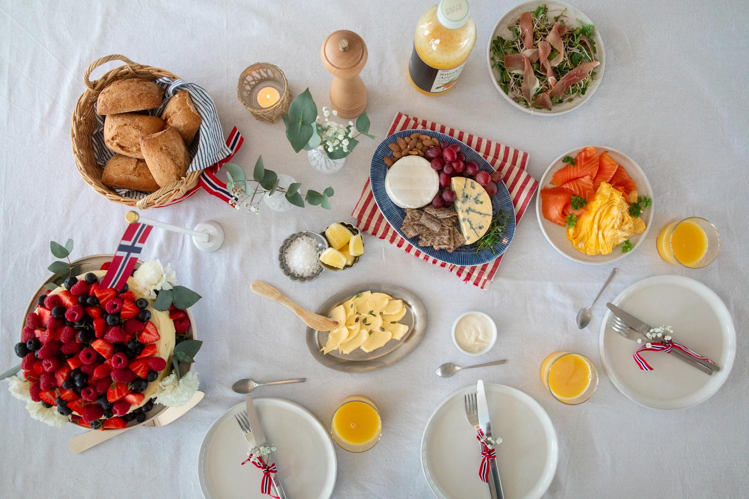 17. mai pyntet frokostbord sett ovenfra med juice, kake, eggerøre, skinke, laks, rundstykker, smør osv.