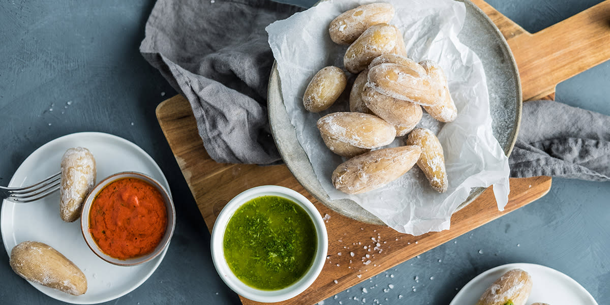 Saltkokte kanaripoteter med saltlag servert på grå tallerken med hvitt bakepapir. Tallerkenen står på trefjøl, og det er to skåler ved siden av, én med rød mojosaus og en med grønn mojosaus.
