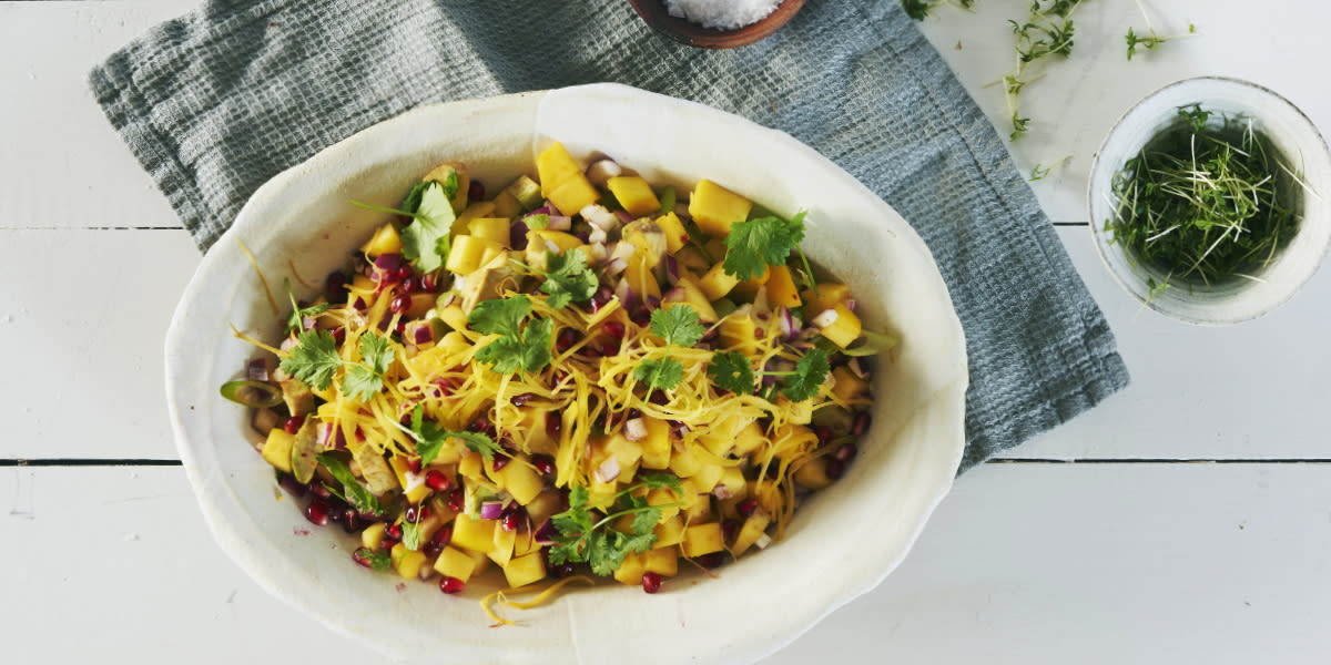 Mango- og avokadosalat med granateplekjerner og fersk koriander, servert i hvit avland skål.