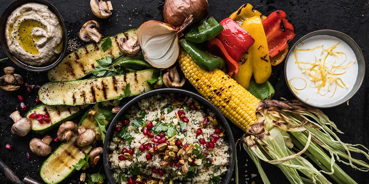 Grillede grønnsaker med baba ganoush og couscoussalat. Skål med sitrondressing på siden. Bordet bugner med forskjellige grillede grønnsaker.