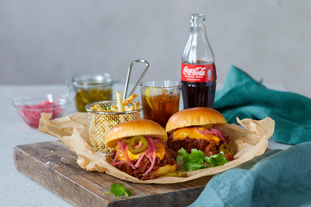 Sloppy joes med syltet rødløk servert med pommes frites og Coca-Cola på en skjærefjøl av mørkt tre.