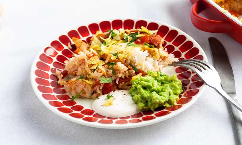 meksikansk kylling med ris og guacamole på en rød tallerken med bestikk