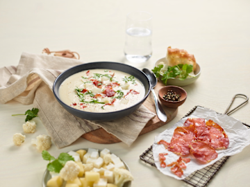 Blomkålsuppe med sprøstekt spekeskinke på siden og grønnsaker på en tallerken