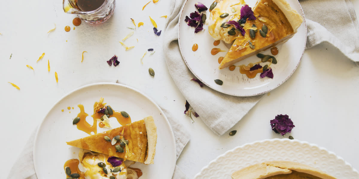 Gresskarpai med høstkrydder servert i stykker på hvite asjetter, pyntet med karamellsaus, iskrem og gresskarfrø.