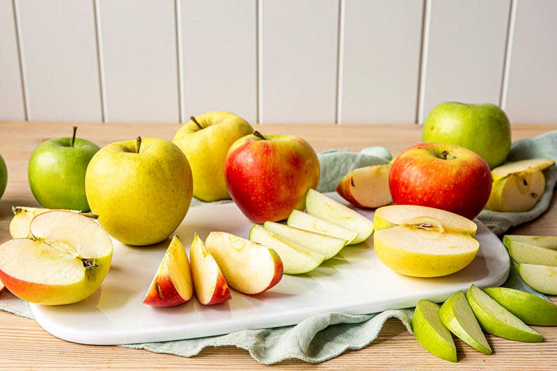 Gule, røde og grønne epler, både hele og delt i båter. Eplene står på en hvit marmorfjøl, med lyseblå linserviett.