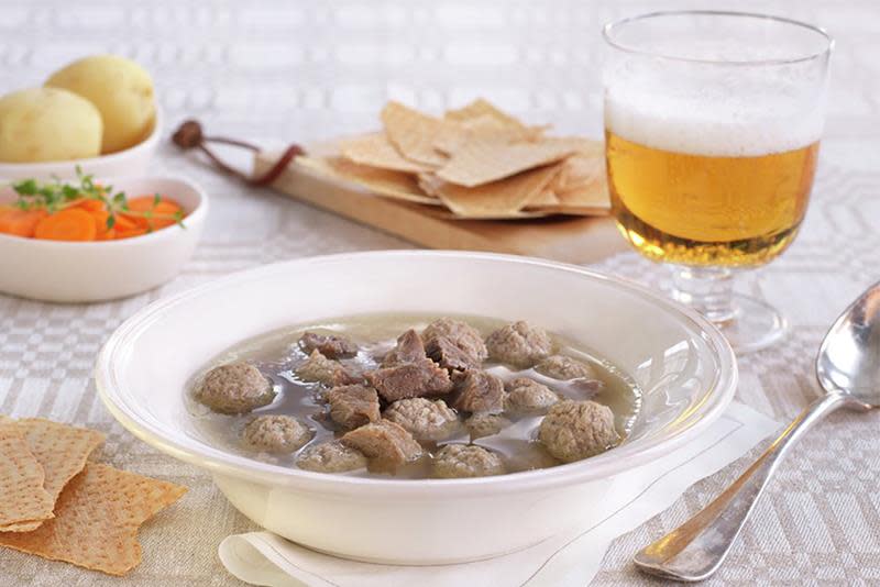 Hjemmelaget sodd, servert i hvit skål, med flatbrød, gulrot, potet og et glass øl på siden.