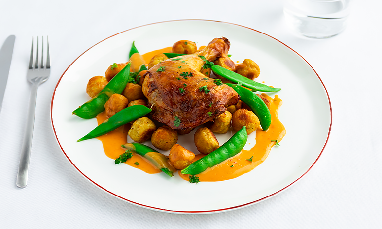 Grillet kyllinglår liggende oppå noisette-poteter, sukkererter, kyllingsaus og en hvit tallerken med rød kant.