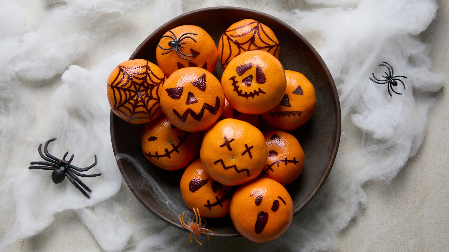 Halloween klementiner servert i svart skål med spindelvev og svarte plastederkopper i bakgrunnen.