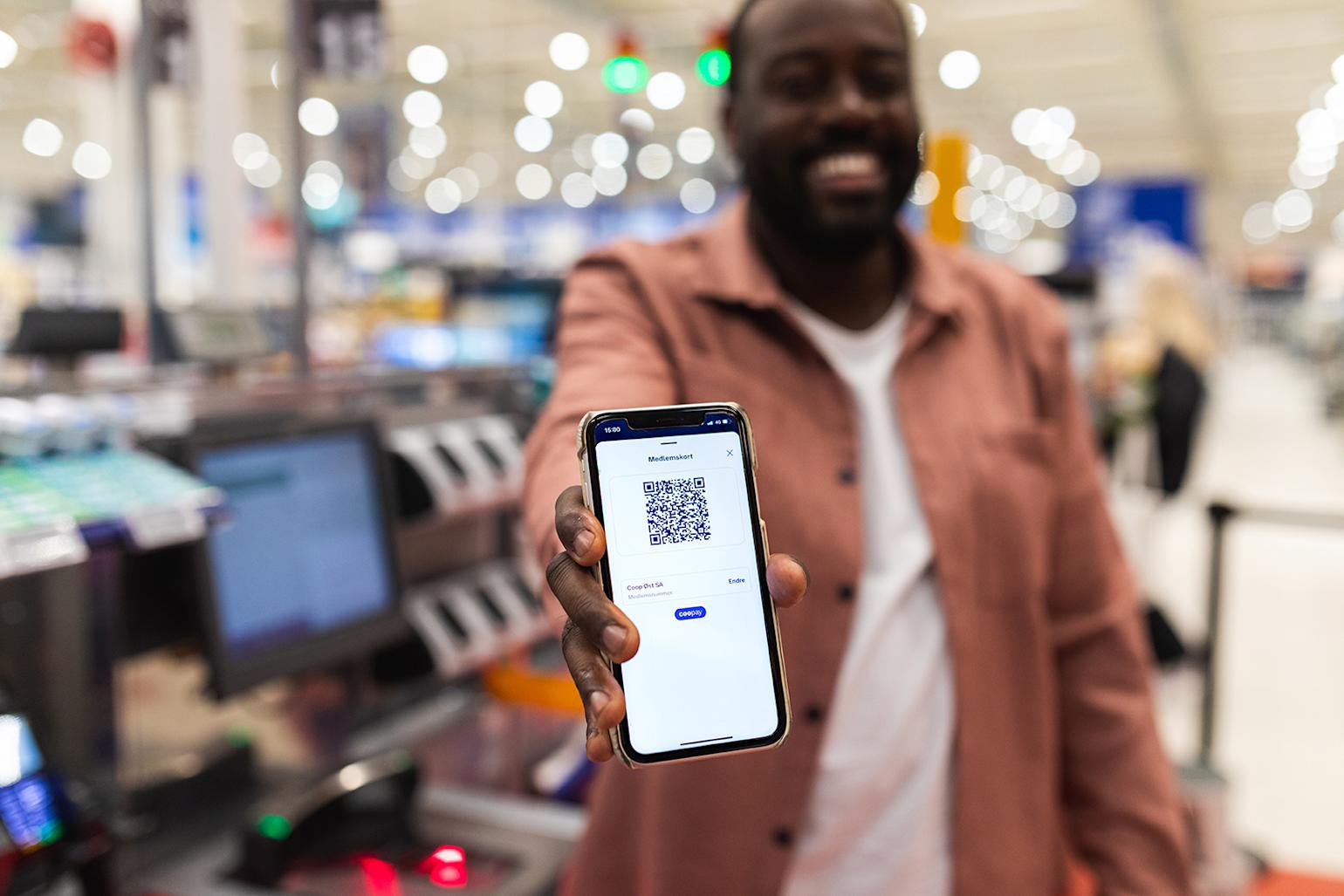 Kunde smiler og viser frem Coop-appen