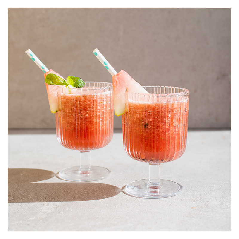 Rød vannmelonslush i to stettglass, pyntet med fersk vannmelon, og stripete sugerør. Sommerlys.