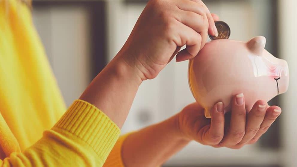 Dame i gul genser legger en mynt på en rosa sparegris.