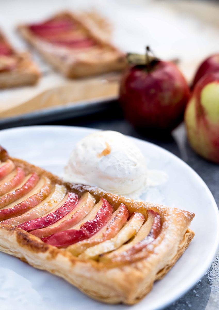 Verdens enkleste epleterte; epleskiver i firkantet skall av butterdeig, servert på hvit tallerken med en kule iskrem. Epler i bakgrunnen.