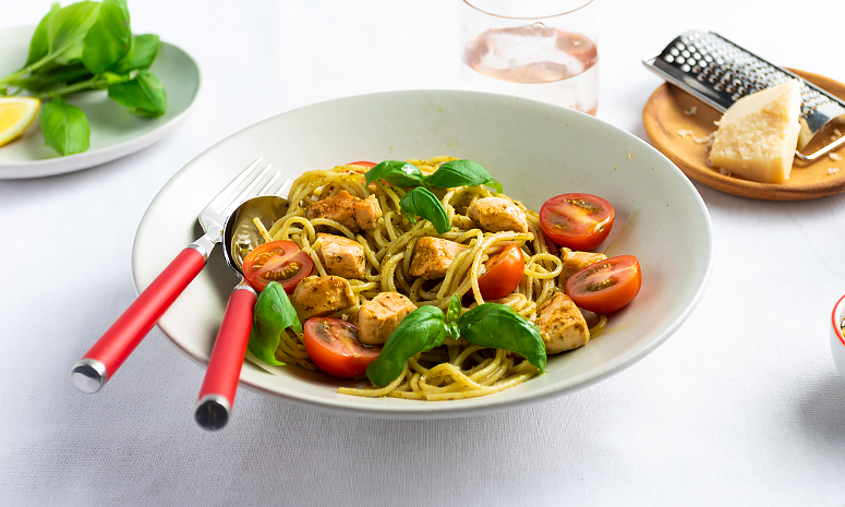Pasta med kylling og tomater toppet med basilikum i en hvit skål.