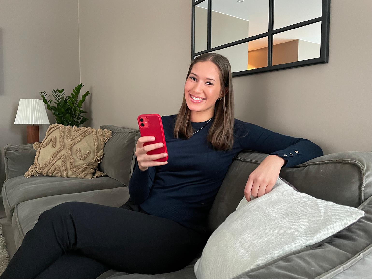 Kvinne smiler med rød telefon i hånden