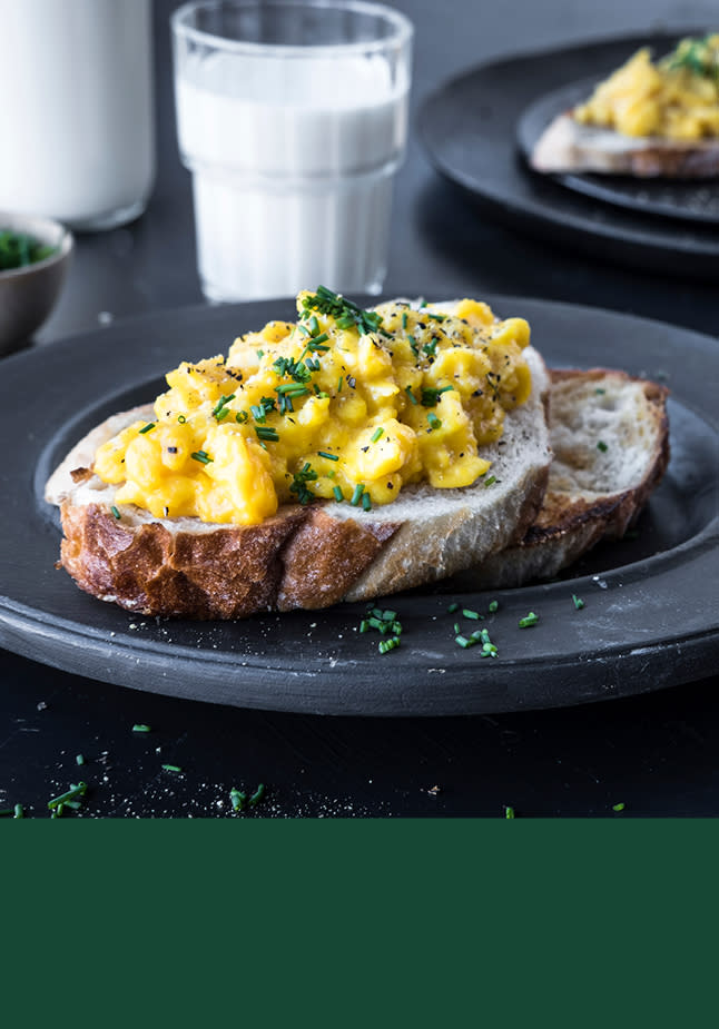 Eggerøre på en brødskive på en sort tallerken. Et glass med melk står i bakgrunnen.