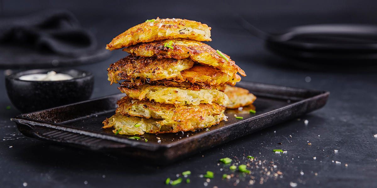 Røstipoteter med parmesan, stablet på fat. Drysset med litt grønne urter. Skål med dip til venstre.
