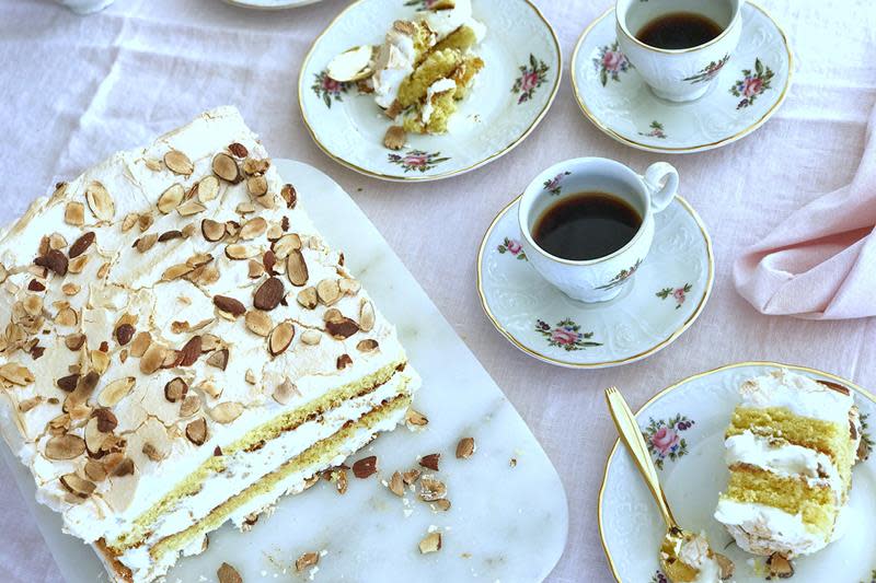 Klassisk Kvæfjordkake servert på hvitt marmorfat, på lys duk. Småblomstret kaffeservise med kaffekopper, og asjetter med biter av kake.