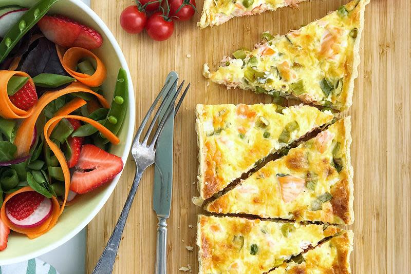 Oppskåret firkantet pai med laks, erter og gressløk. Servert på trefjøl, med frisk salat ved siden av.