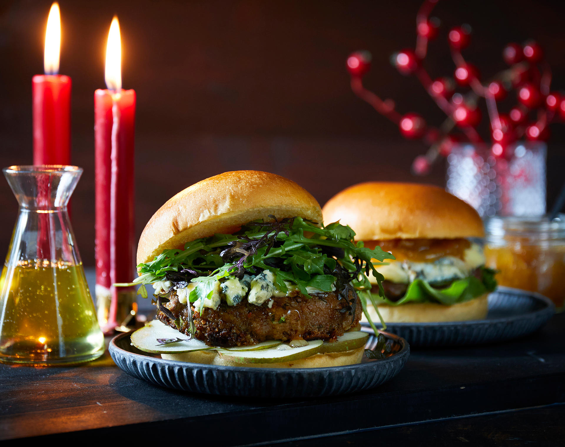 Valnøttburger med blåmuggost, honning og pærer, servert med ruccolamiks på liten mørkegrå tallerken. Burgeren står på juledekket bord sammen med en burger med blåmuggost og fikenmarmelade.