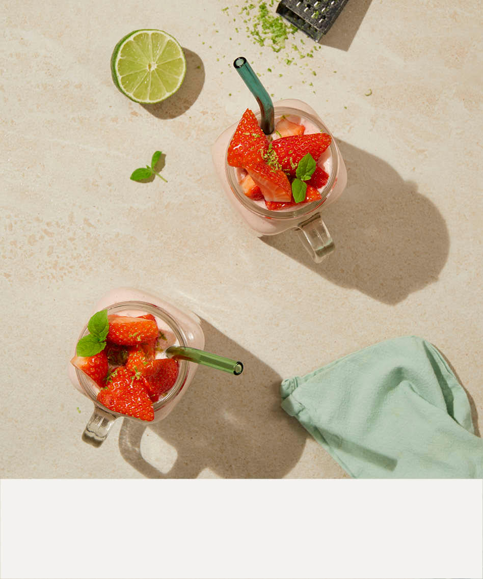 Rød drink med grønt sugerør, lime og rivehjern og beige stripe nederst